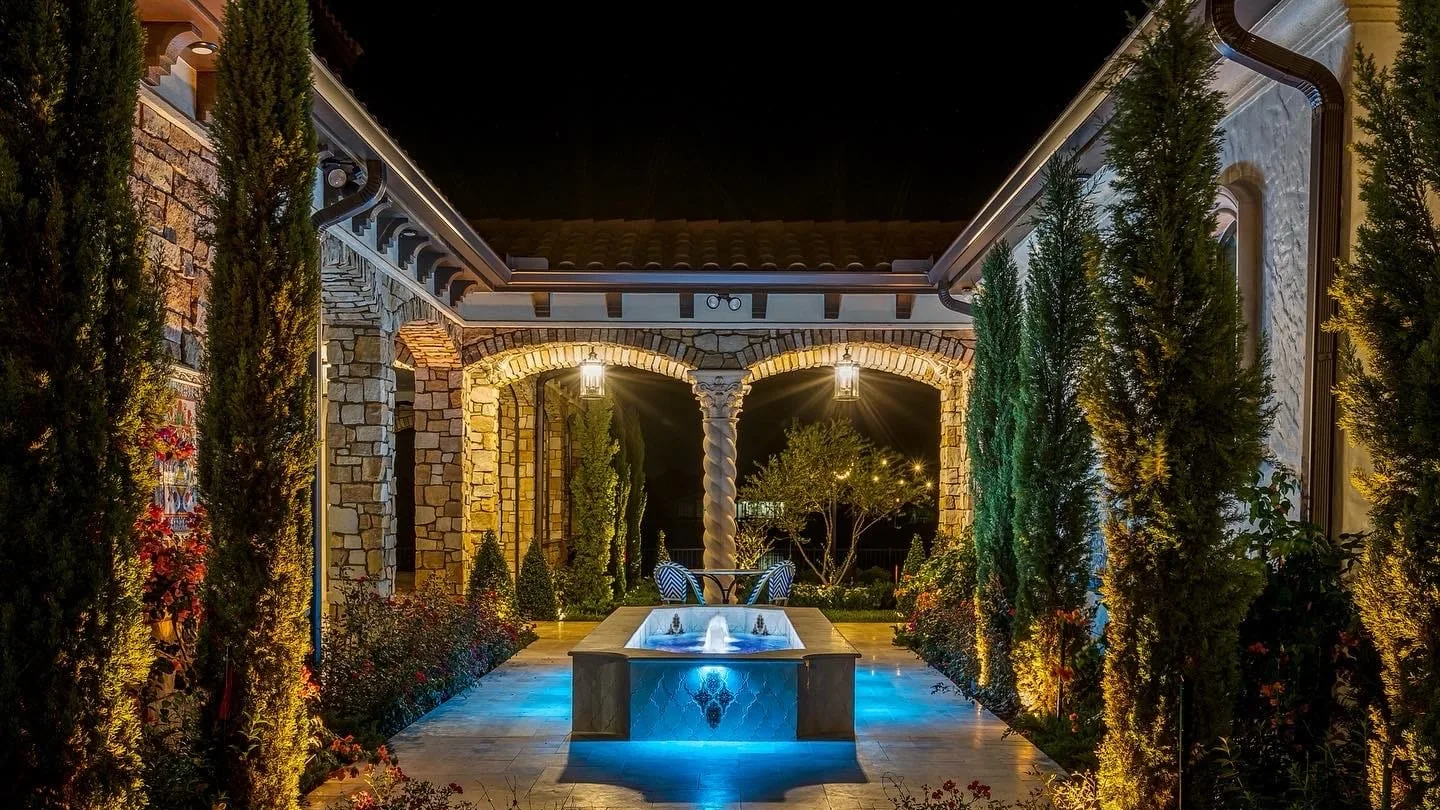 Natural stone arched loggia with a twisted column around a courtyard fountain at night, stone masonry