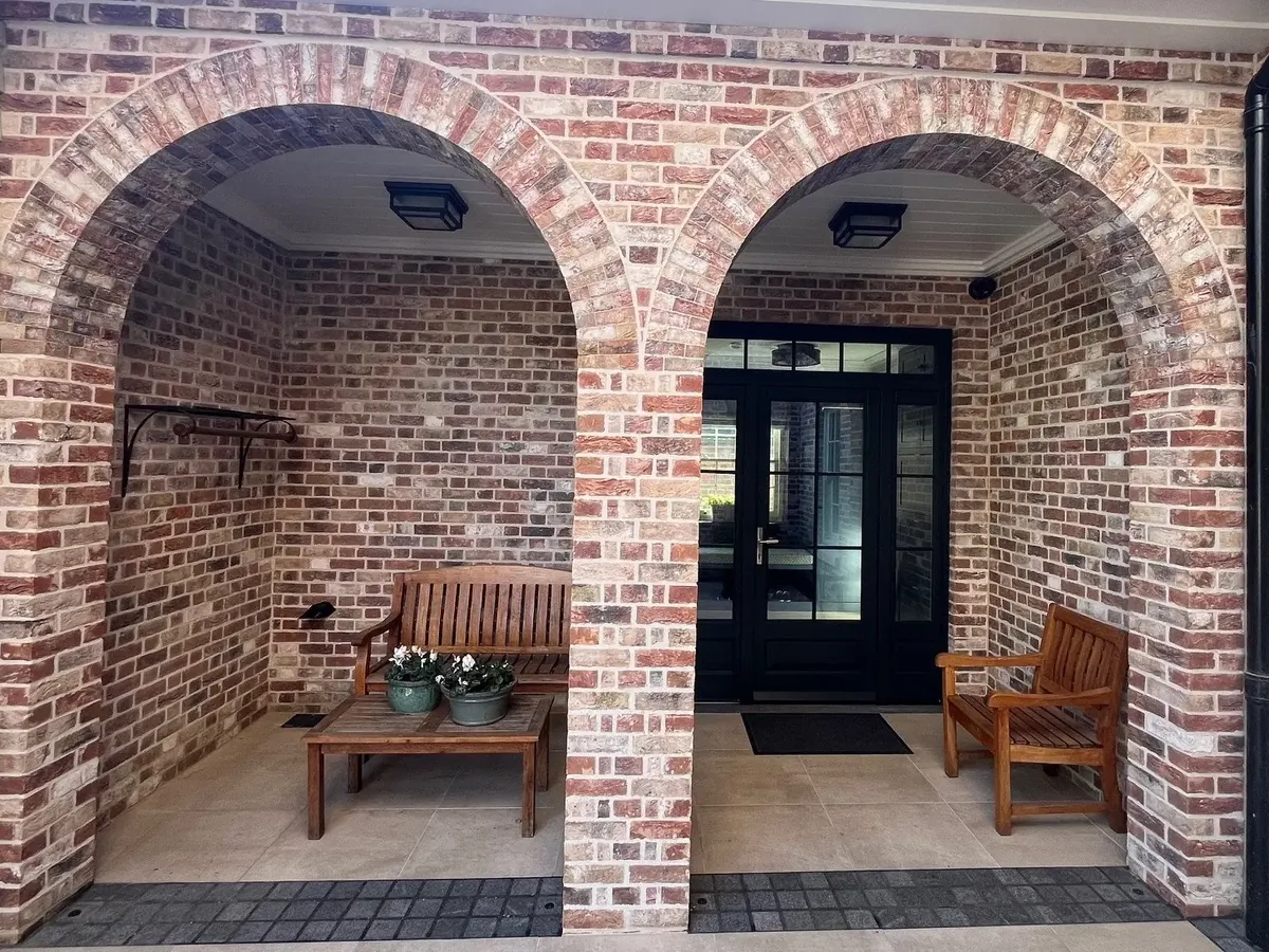 Two brick arches framing a covered entry porch with benches, brick masonry