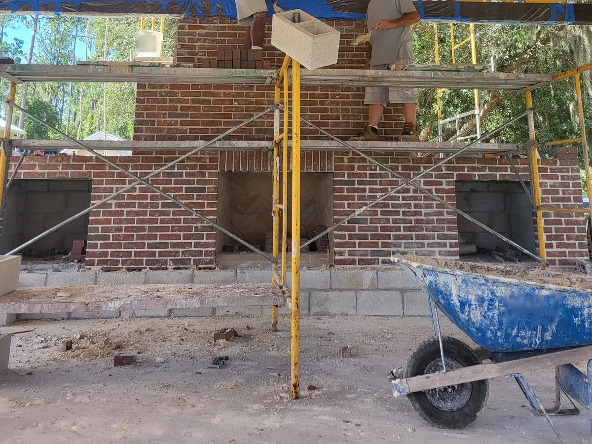 Red brick fireplace wall with a herringbone firebox and two side niches going up on scaffolding, brick masonry