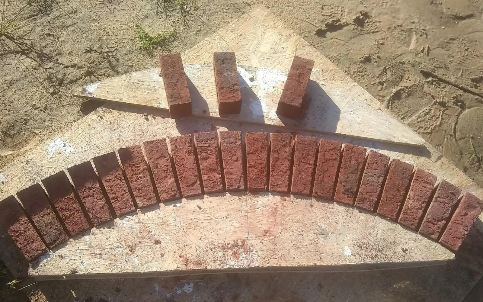 Brick masonry: cut brick arch pieces laid out in a curve on a plywood arch template before setting