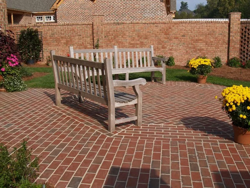 Clay brick patio in a herringbone pattern with a soldier course border and two wooden benches, brick pavers