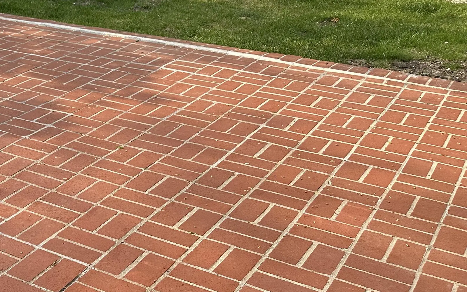 Brick pavers: clay brick patio in a basketweave pattern with mortar joints beside a lawn