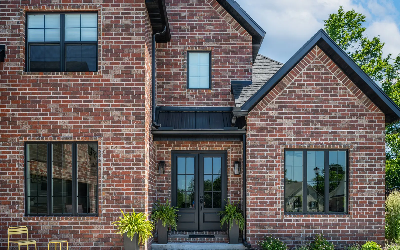 Brick veneer: red brick house front with black windows, a double front door and two gables