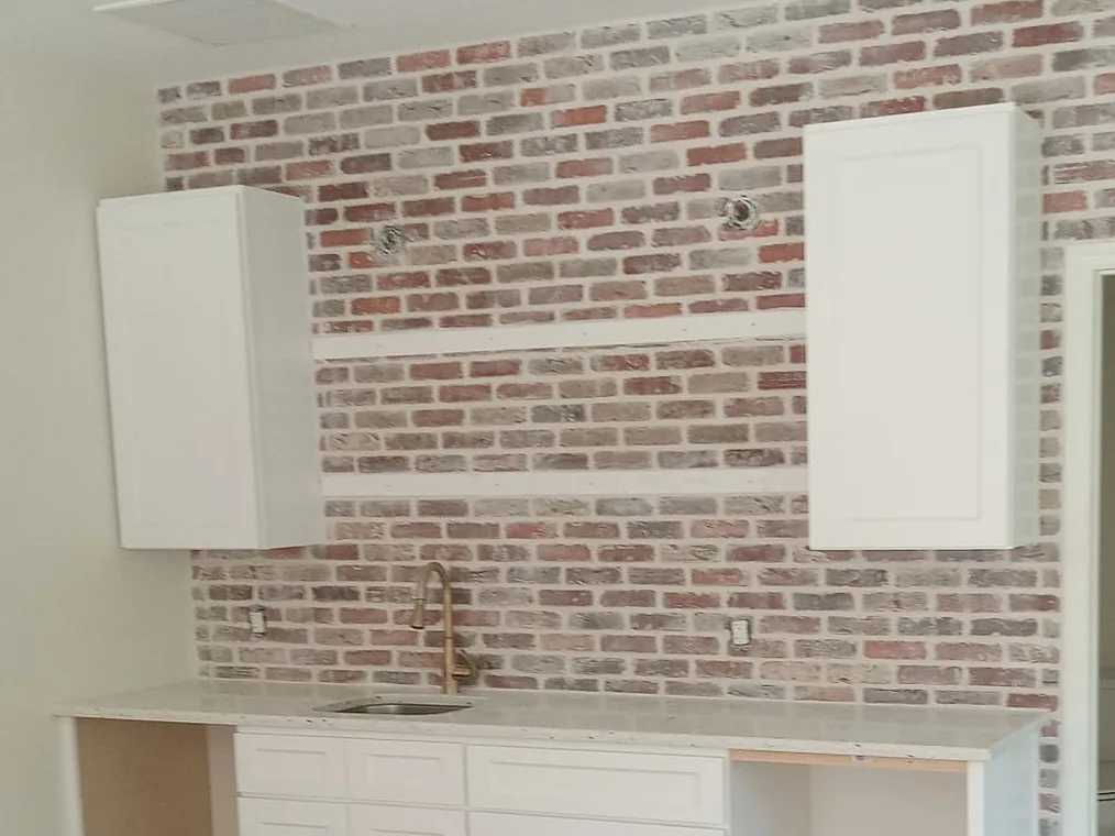 Interior kitchen wall in whitewashed brick above white cabinets and a stone countertop, brick veneer