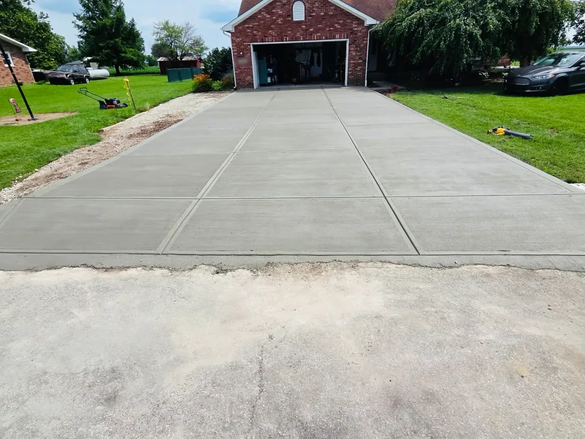 New gray broom-finish concrete driveway with control joints leading to a brick house garage, concrete driveways and patios