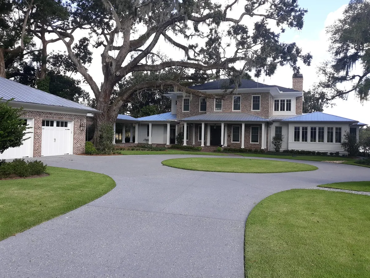 Charcoal concrete driveway curving around a round lawn island to a two-story brick house under a live oak, concrete driveways and patios
