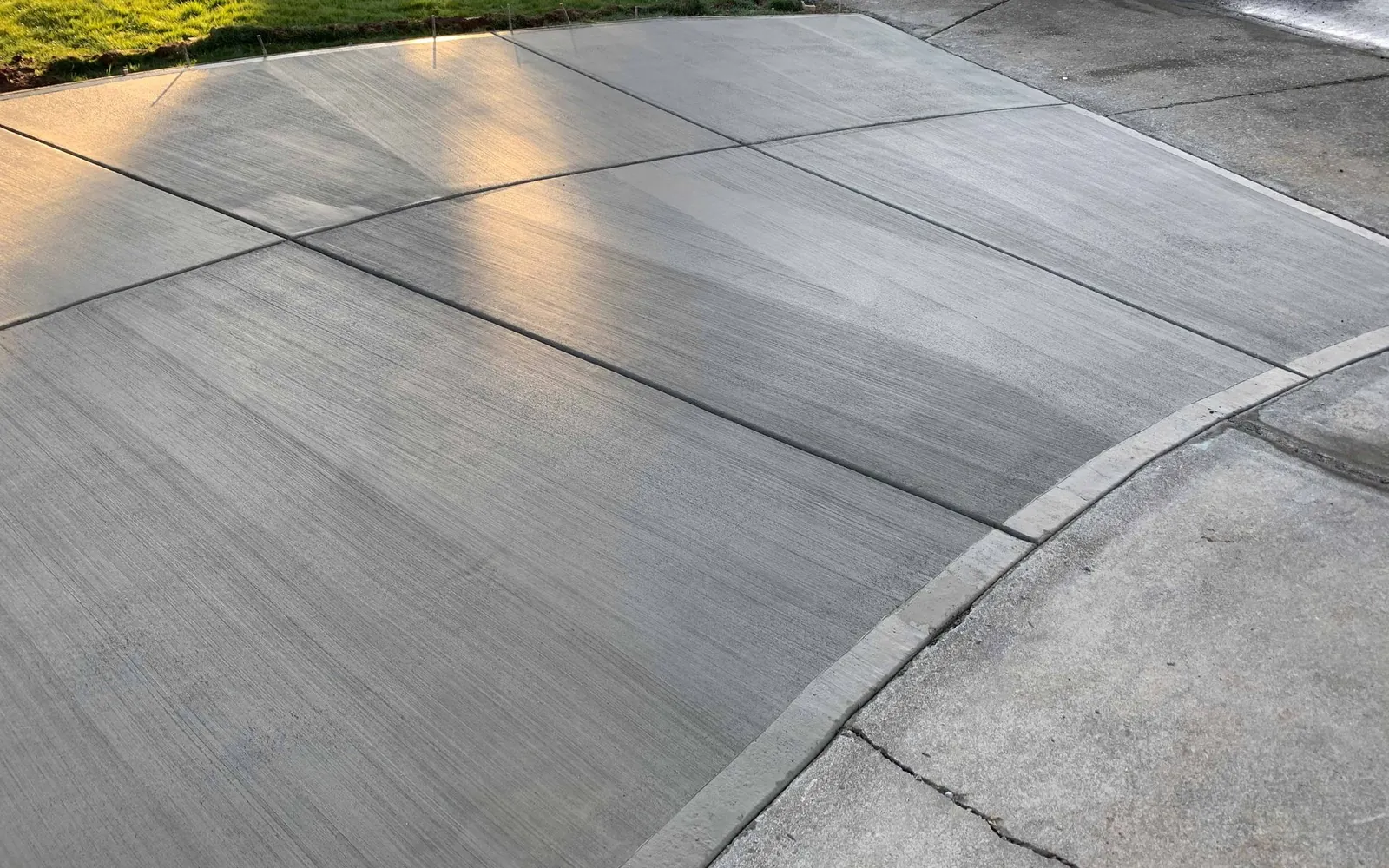 Concrete driveways and patios: new broom-finish concrete driveway with tooled control joints curving past a lawn