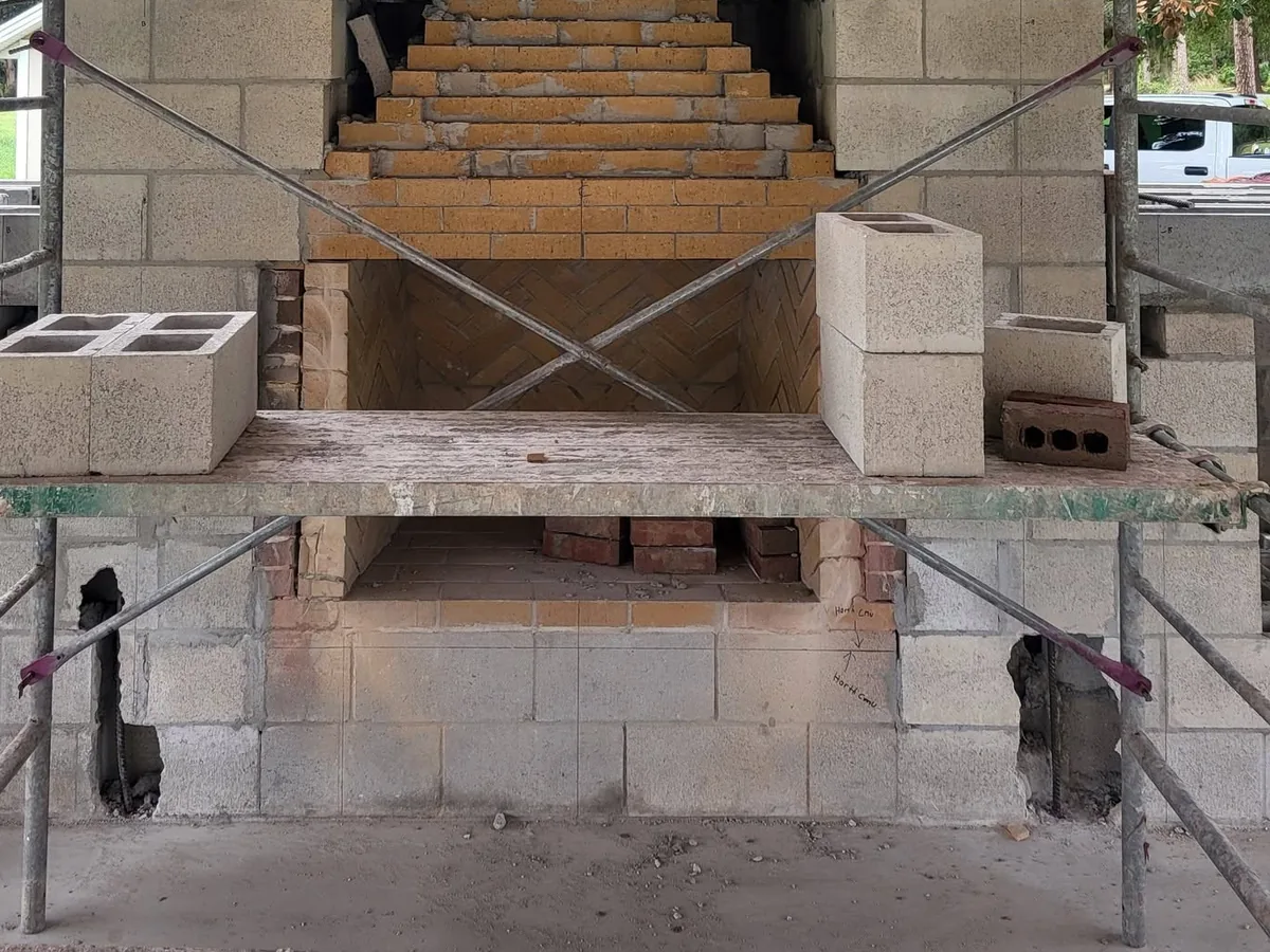 Masonry fireplace under construction: a herringbone firebrick firebox with the firebrick smoke chamber corbelled in above it, inside a concrete block core