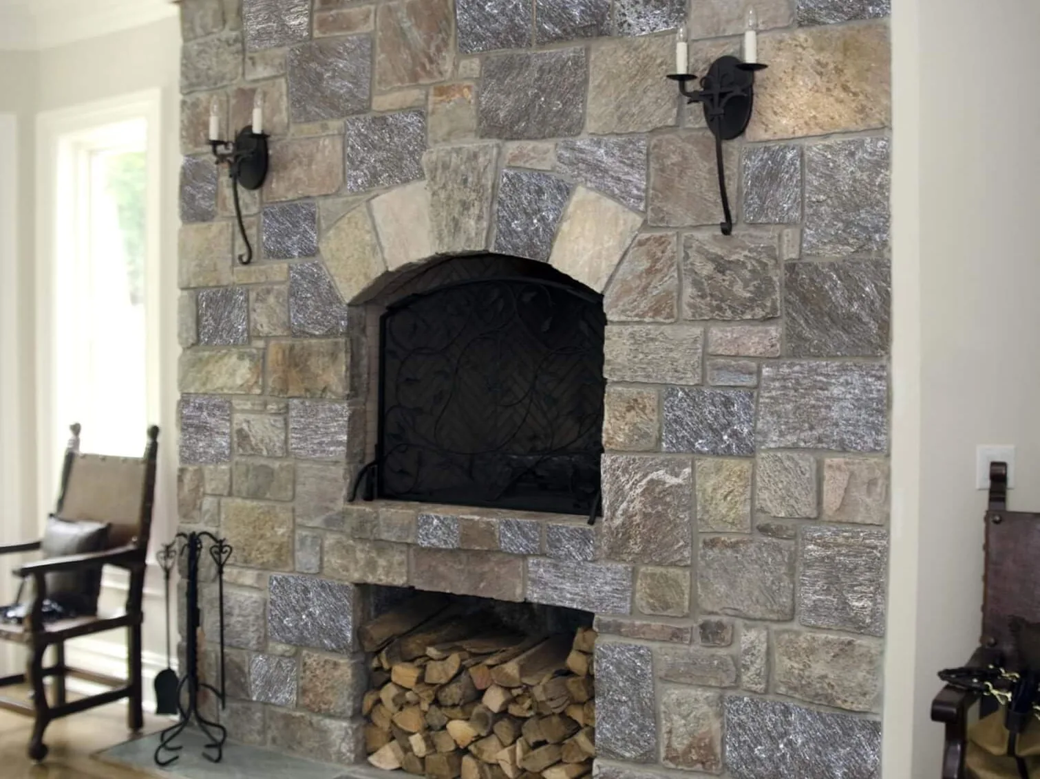 Indoor fireplaces: natural stone fireplace with an arched firebox opening, an iron screen and a log niche below