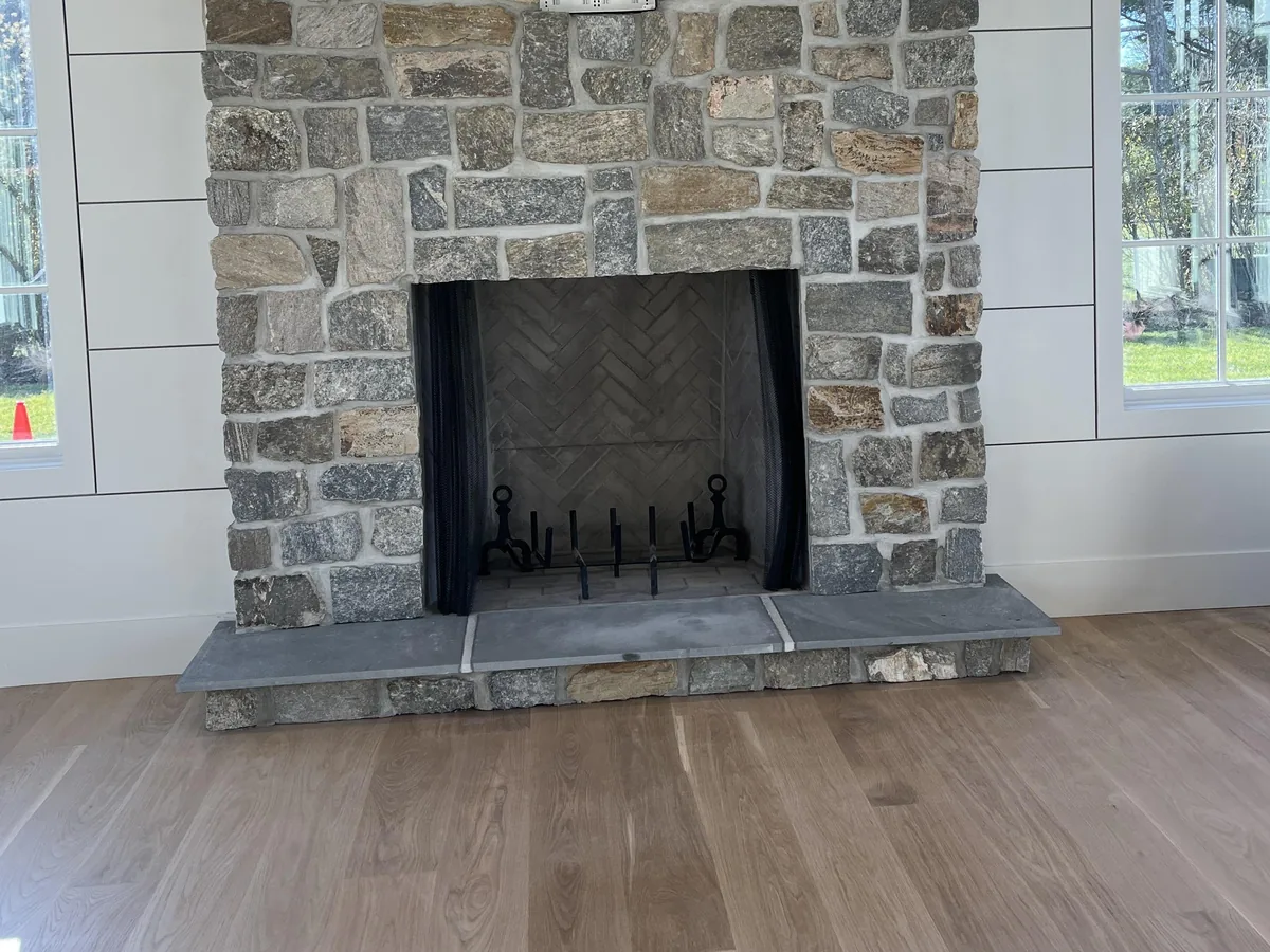 Natural stone fireplace with a herringbone firebrick firebox, andirons and a bluestone hearth in a new living room, indoor fireplaces