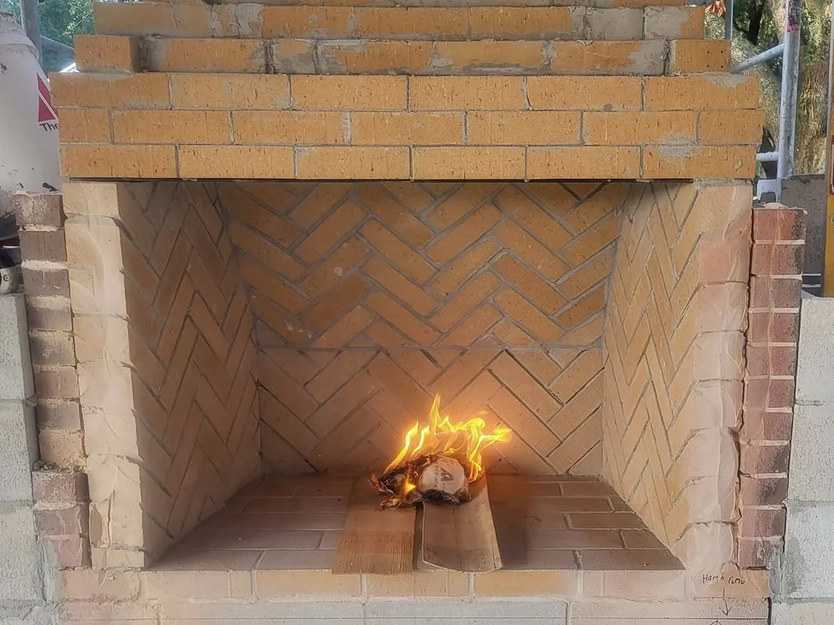 Fire burning in a new herringbone firebrick firebox with a firebrick hearth, built on a concrete block core, outdoor fireplaces