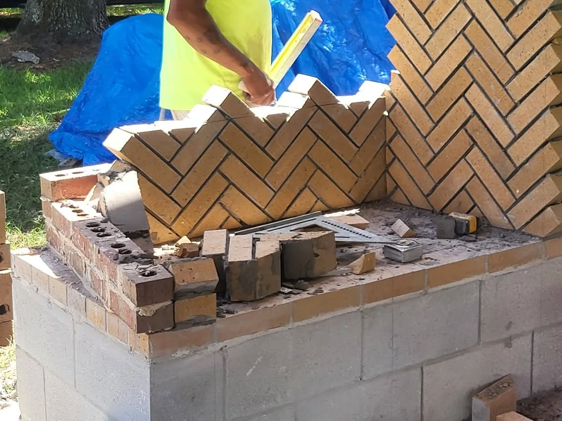 Mason laying herringbone firebrick for an outdoor fireplace firebox on a concrete block base, outdoor fireplaces