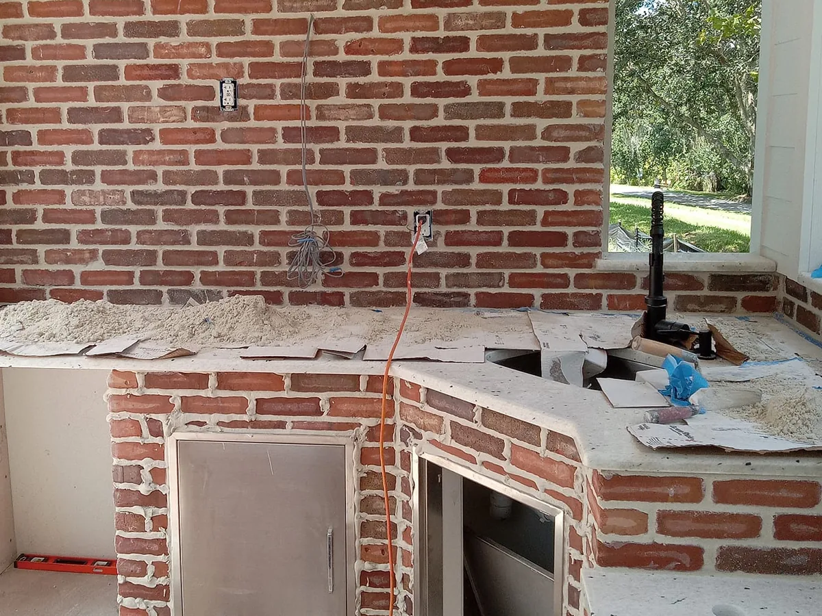 Brick base of an outdoor kitchen before the whitewash, with a stainless access door, a refrigerator opening and the counters set, outdoor kitchens