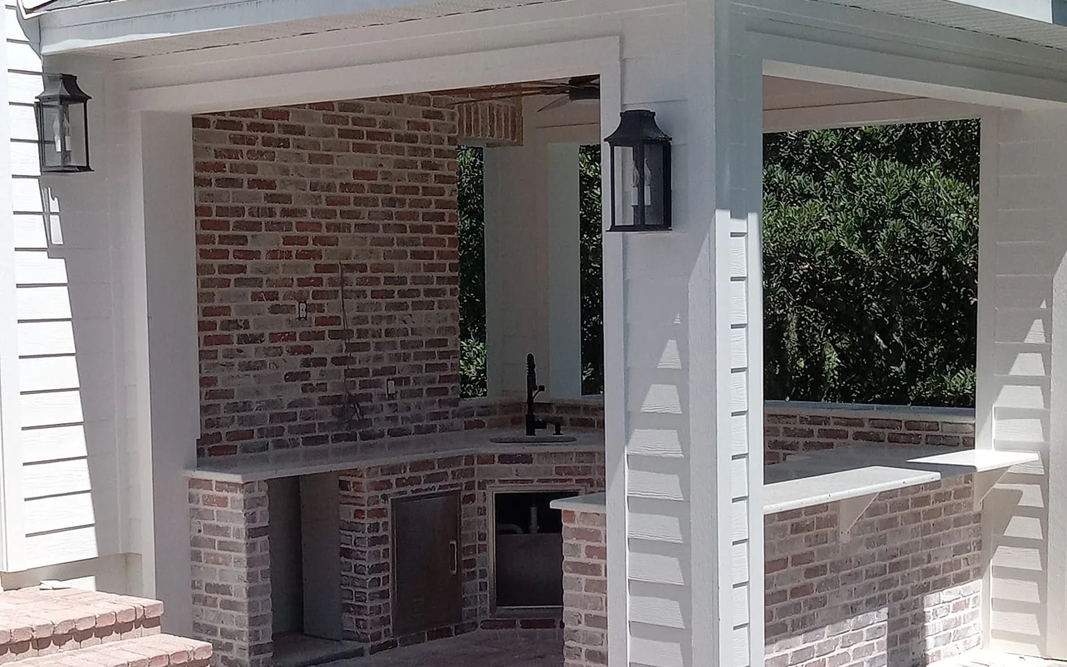 Outdoor kitchens: whitewashed brick outdoor kitchen with a bar-height wall, a sink and lantern lights on a covered porch beside a pool
