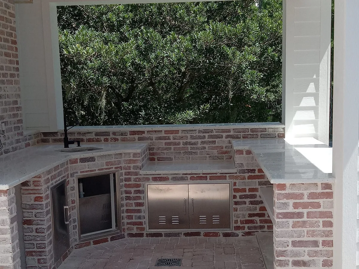 U-shaped outdoor kitchen in whitewashed brick with stone countertops, a sink and stainless access doors on a covered porch, outdoor kitchens