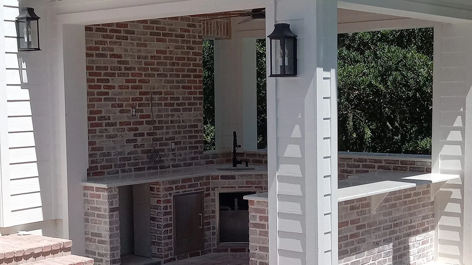 Whitewashed brick outdoor kitchen with a sink and lantern lights on a covered porch beside a pool, masonry