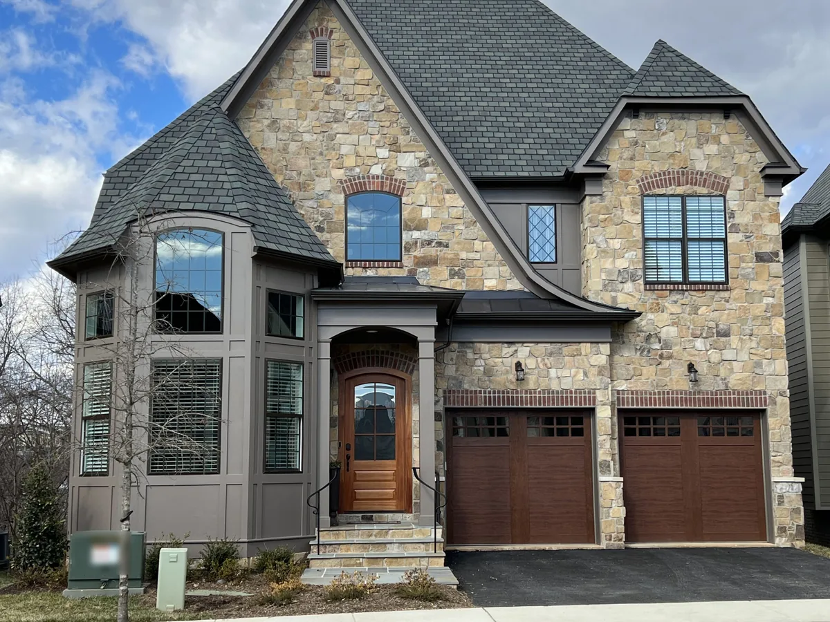 Two-story house faced in natural stone veneer with a rounded bay and an arched front door, stone masonry