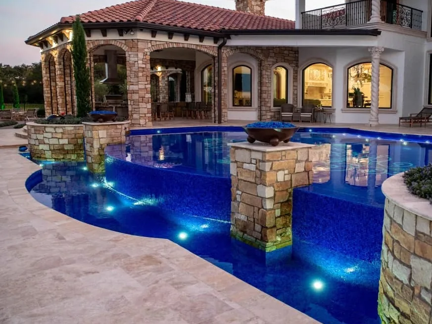 Pool with natural stone columns rising from the water in front of a stone arched loggia, stone masonry